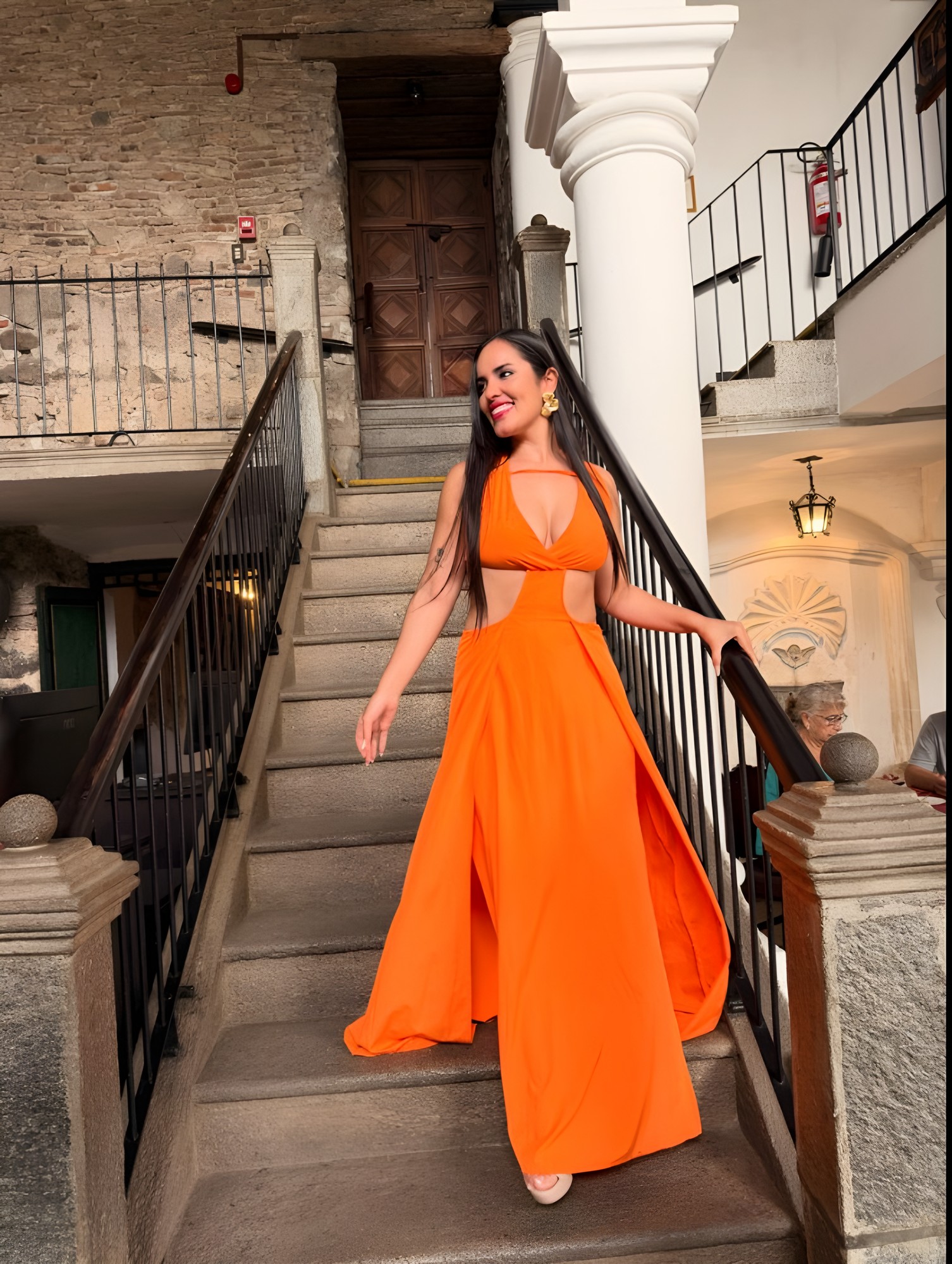 Mariel con vestido naranja bajando una escalera colonial